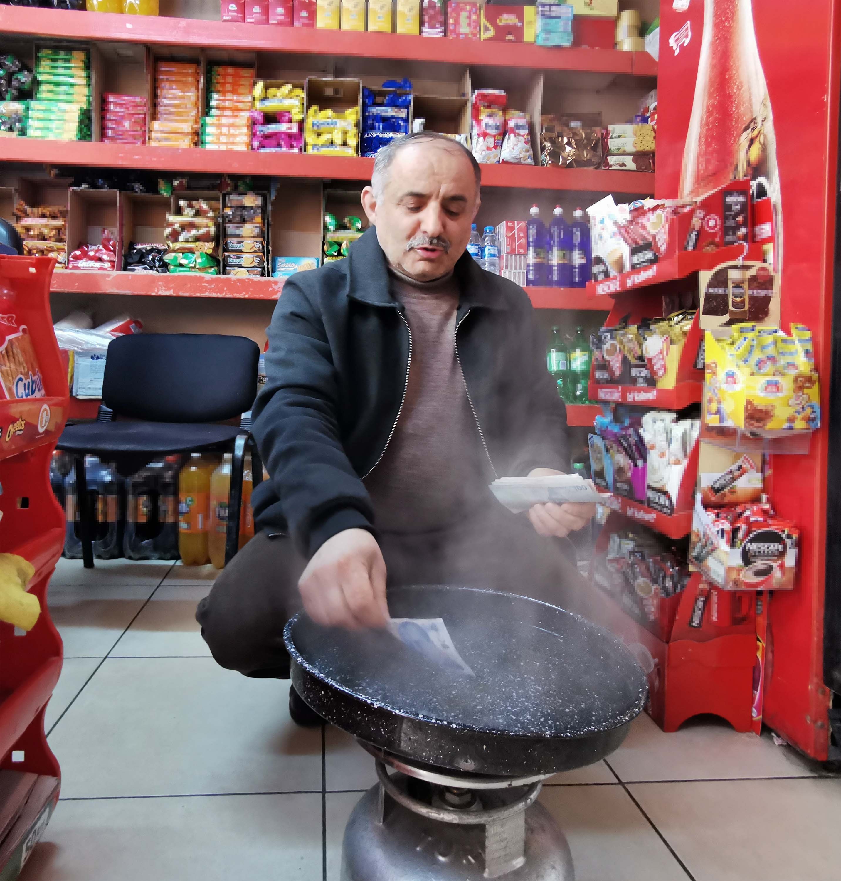 Orhan Sarı, a grocer from northern Ordu province, sterilizes the money he received from customers in an innovative way, May 4, 2020. (DHA Photo)