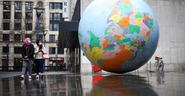 People wearing protective face masks walk past "The World Turned Upside Down" sculpture by Mark Wallinger, London, Britain, Jan. 20, 2021. (Reuters Photo)