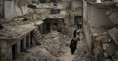 Women walk in a neighborhood heavily damaged by airstrikes in Idlib, northwestern Syria, March 12, 2020. (AP Photo)