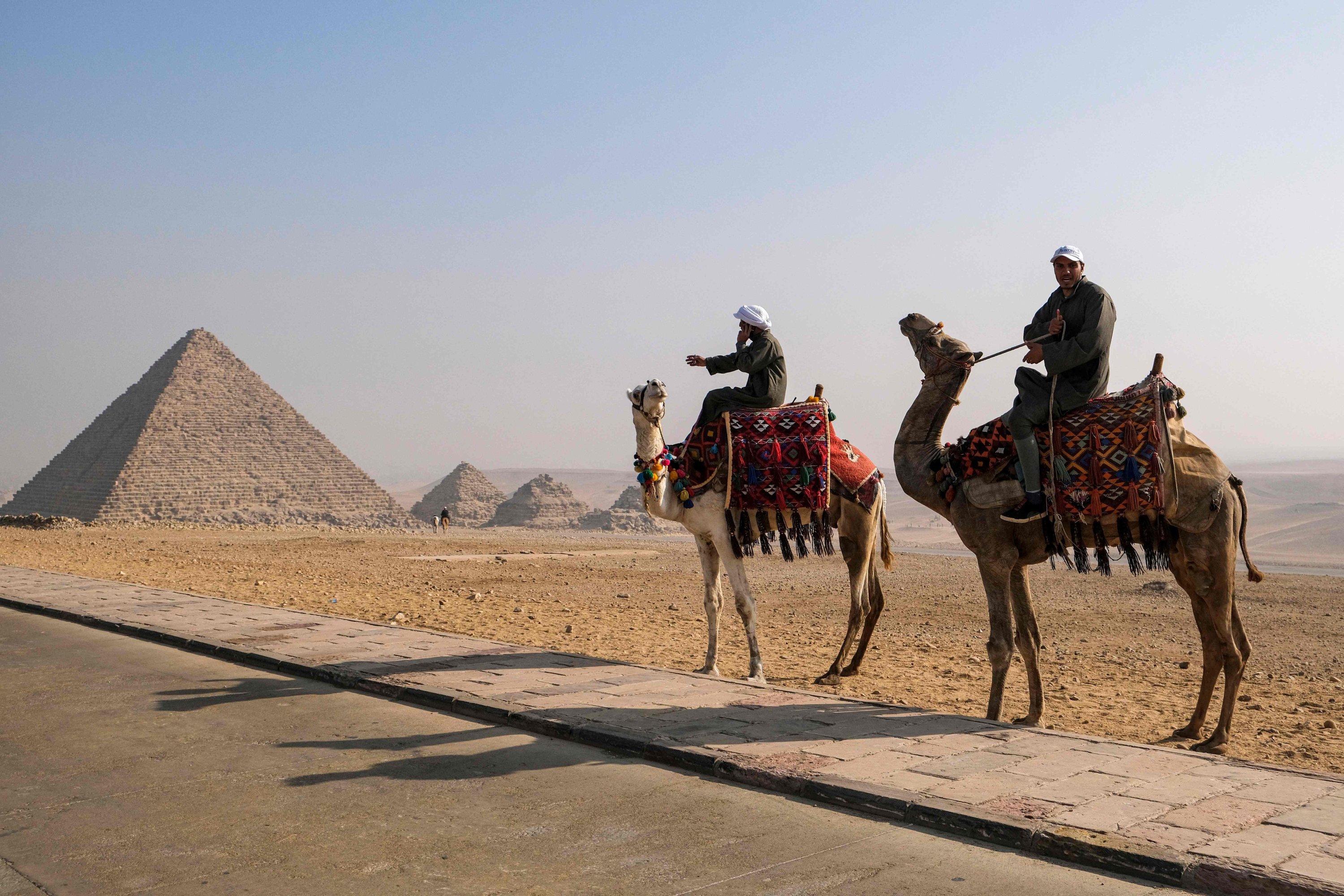 Camel trainers ride camels awaiting tourists by the Pyramid of Menkaure (Menkheres) at the Giza Pyramids Necropolis on the western outskirts of the capital