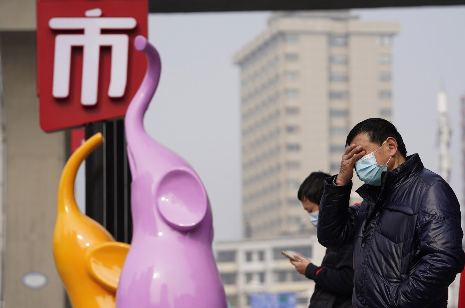 Residents wearing masks to curb the spread of the coronavirus stand near the Chinese character for "Market" in Wuhan, China, Jan. 26, 2021. (AP Photo)