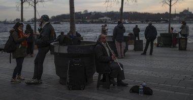 A musician performs while people promenade at the seaside of Karaköy, Beyoğlu, Istanbul, Turkey, Jan. 22, 2021. (AP Photo)