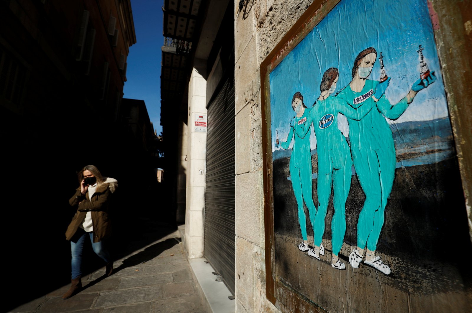 A woman wearing a protective face mask walks past a painting representing the Moderna, Pfizer and AstraZeneca vaccines on Bisbe street in Barcelona, Spain, Jan. 27, 2021. (Reuters Photo)