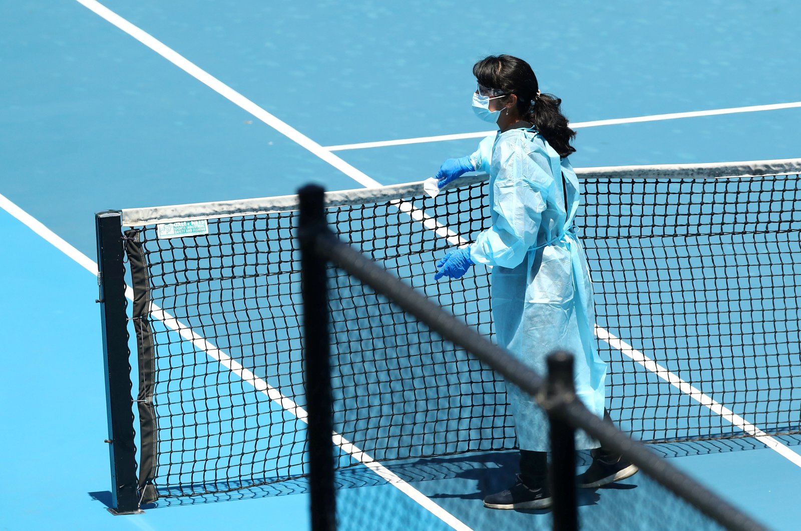 A member of staff wearing PPE cleans the net at Melbourne Park in between the training sessions of tennis players undergoing mandatory quarantine ahead of the Australian Open in Melbourne, Australia, Jan. 21, 2021. (Reuters Photo)