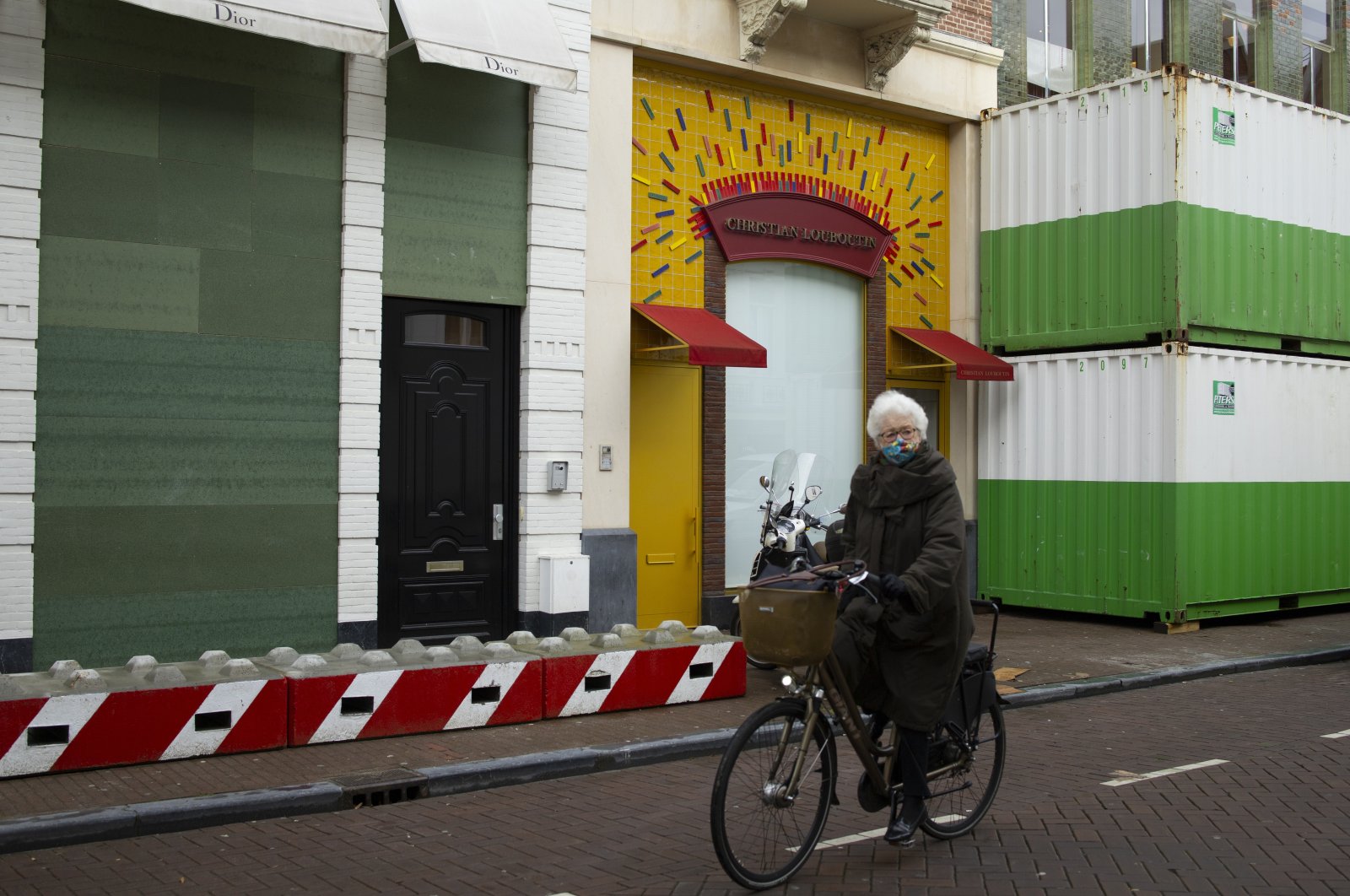 A woman cycles past luxury goods stores that are boarded up, protected by concrete blocks and sea containers at P.C. Hooft street in Amsterdam, the Netherlands, Friday, Jan. 29, 2021. (AP Photo)