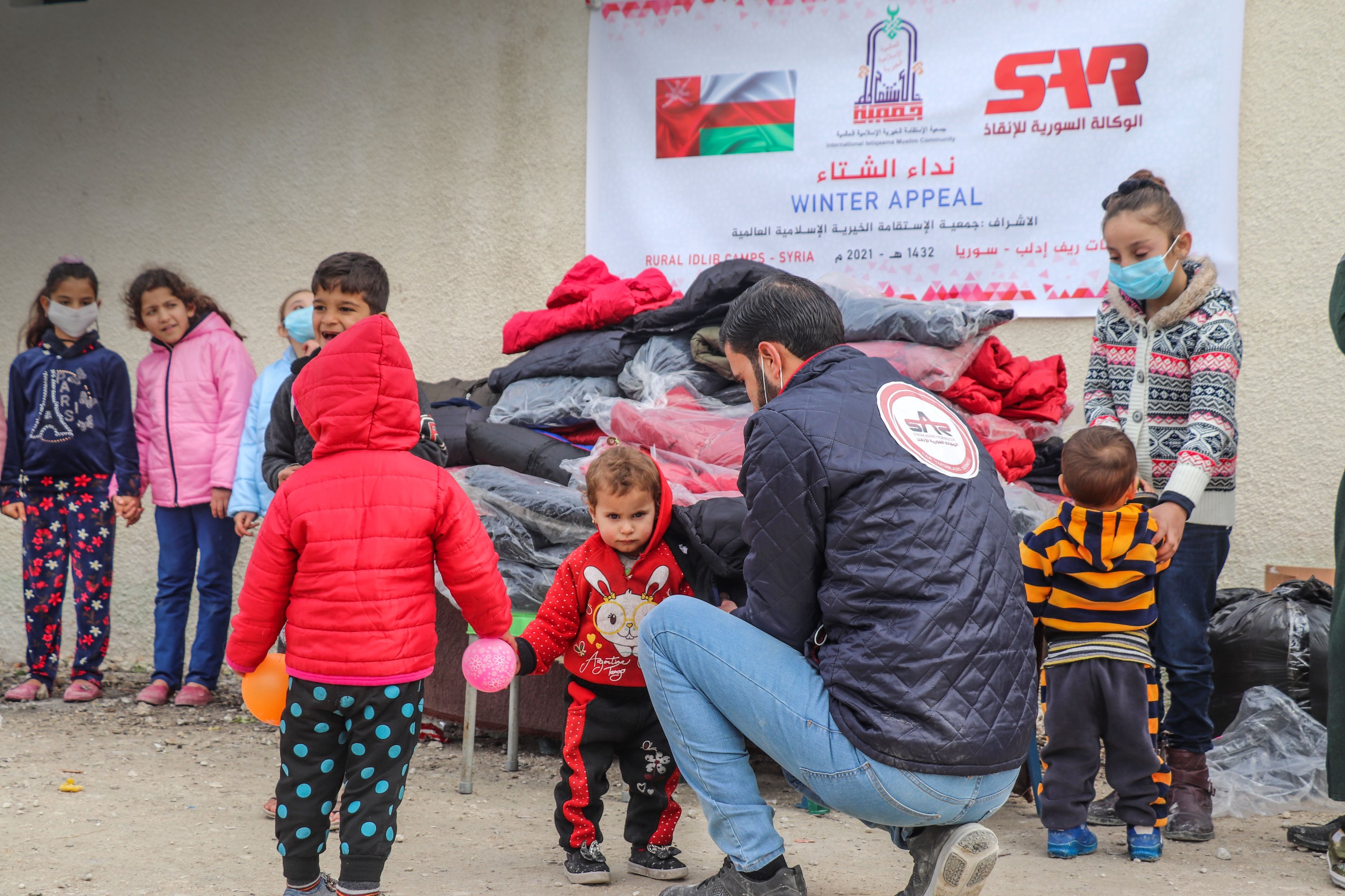 A Sar aid association personnel helps Syrian children to wear their new coats, Feb.1, 2021. (AA)

