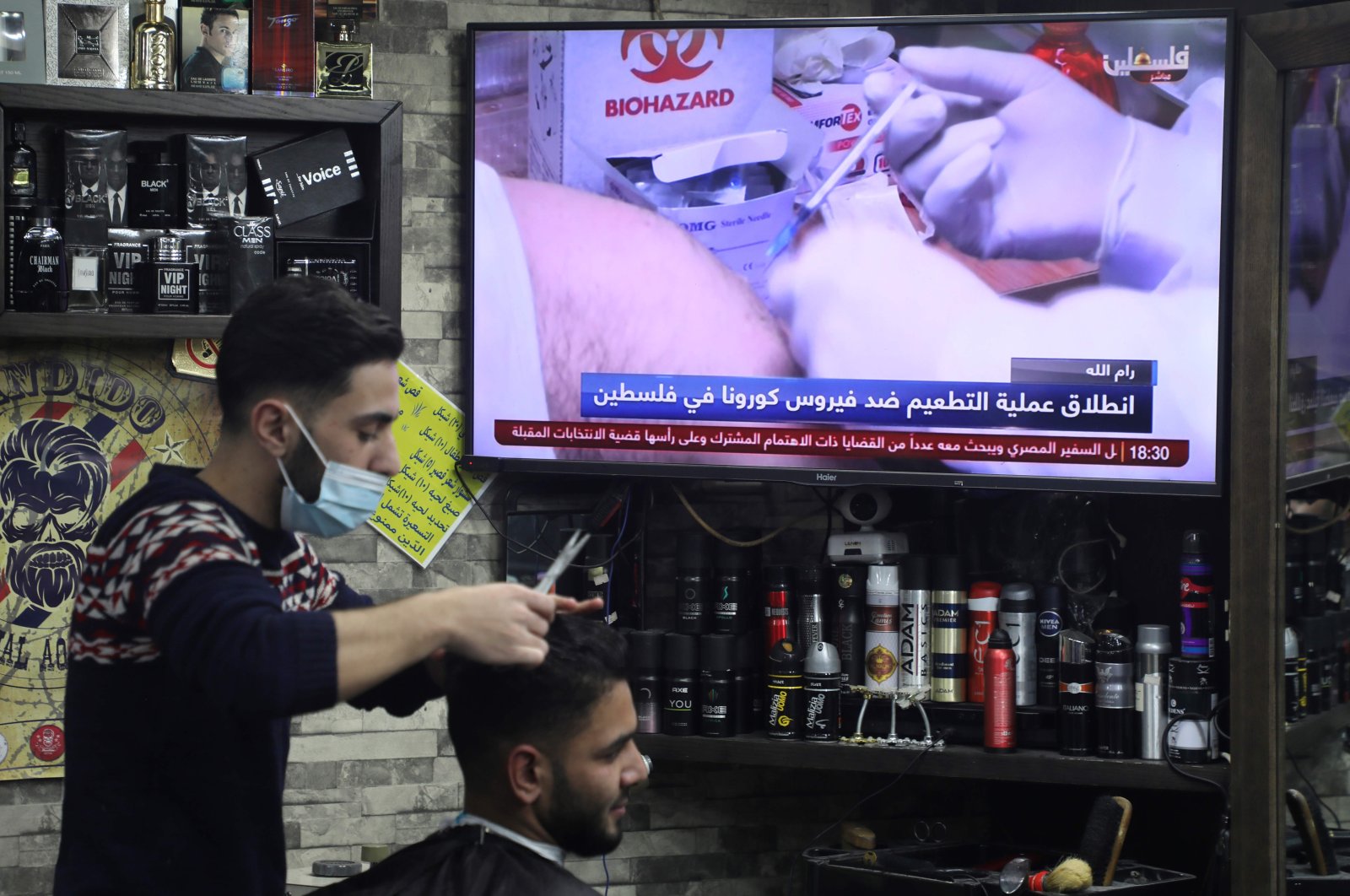 A barber works while watching a live television broadcast of Palestinian health workers getting vaccinated against COVID-19, in Nablus, occupied West Bank, Feb. 2, 2021. (AFP Photo)