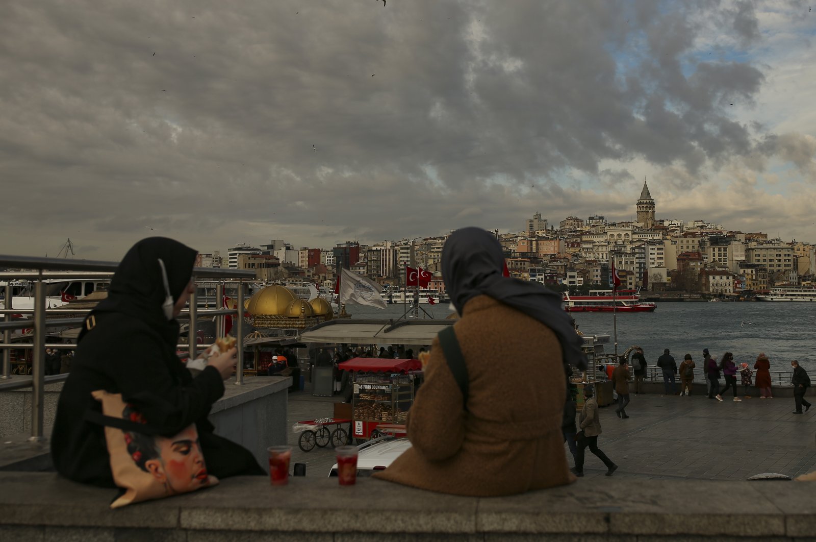 Two women sit near the Galata Bridge hours before a two-day weekend lockdown, Istanbul, Turkey, Jan. 29, 2021. (AP Photo)