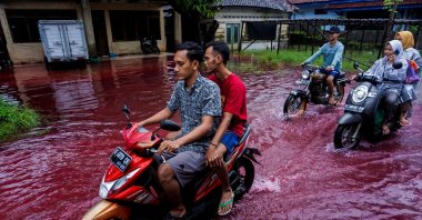 People ride motorbikes through a flooded road with red water due to the dye-waste from cloth factories, in Pekalongan, Central Java province, Indonesia, Feb. 6, 2021. (Reuters Photo)