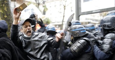 Riot police officers charge a man holding his phone during a protest in Paris, France, Dec. 12, 2020. (AP Photo)