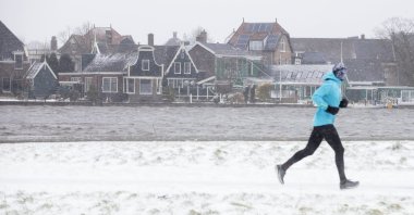 A man exercises along Zaanse Schans river in Zaandam, as snow and strong winds blanketed the Netherlands, Sunday, Feb. 7, 2021. (AP Photo)
