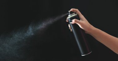 Hand using a spray, isolated on a black background. (Shutterstock Photo)