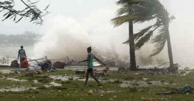 Local residents walk past debris as a wave breaks nearby in Port Vila, the capital city of the Pacific island nation of Vanuatu March 14, 2015. (UNICEF Pacific via Reuters)
