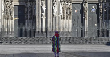 A man in a clown costume stands alone in front of the cathedral when normally tens of thousands of revelers dressed in carnival costumes would celebrate the start of the street carnival in Cologne, Germany, Feb. 11, 2021. (AP Photo)