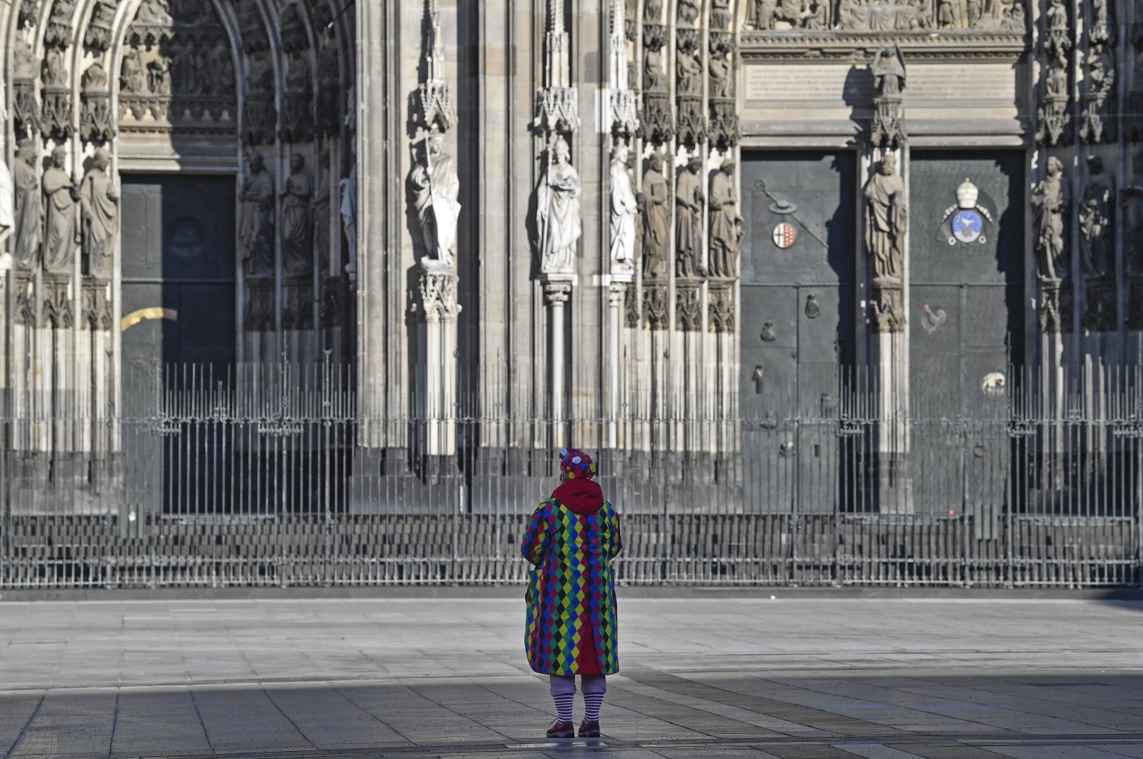 A man in a clown costume stands alone in front of the cathedral when normally tens of thousands of revelers dressed in carnival costumes would celebrate the start of the street carnival in Cologne, Germany, Feb. 11, 2021. (AP Photo)