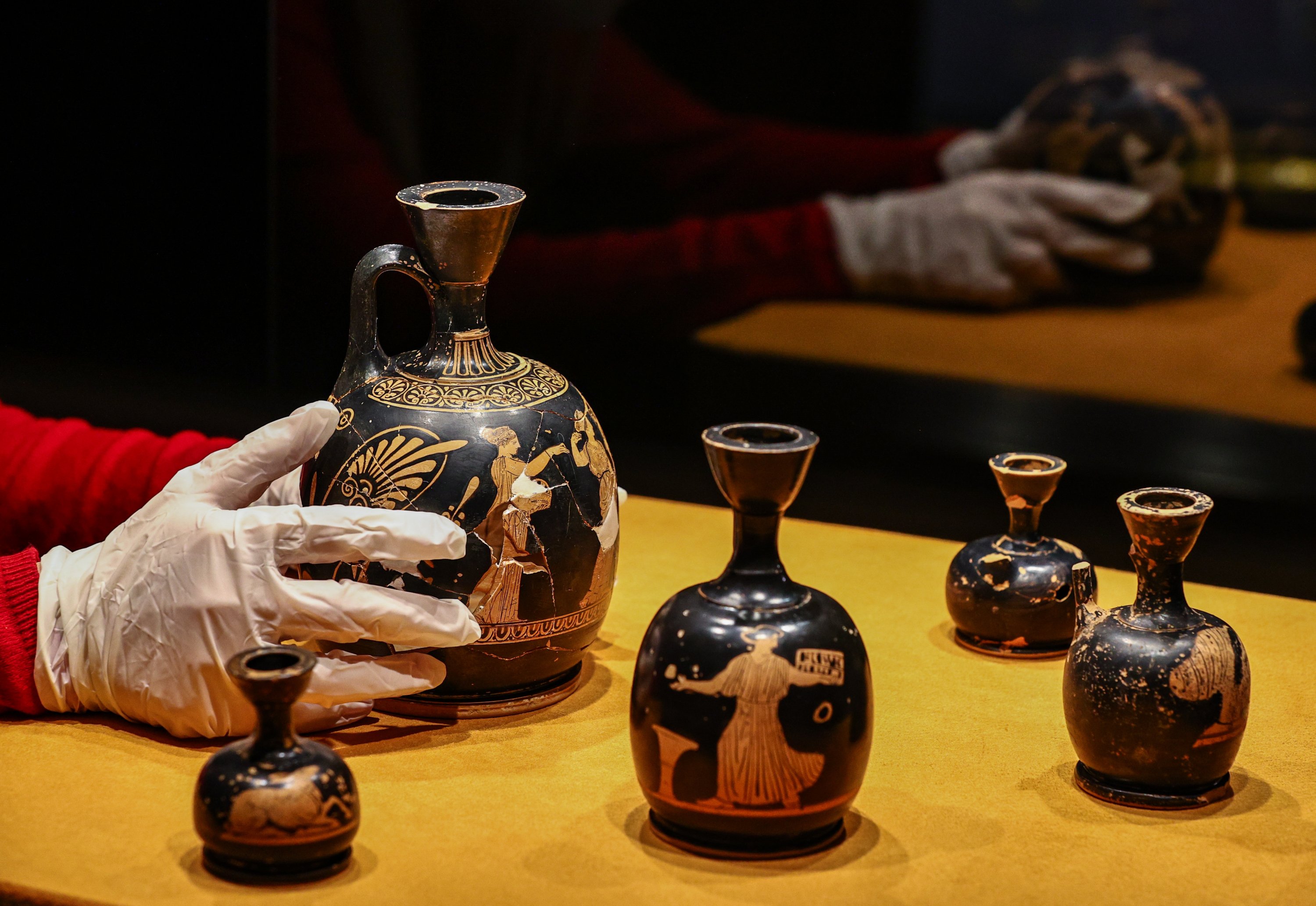 An attendant places an ancient perfume bottle among others on display at the Izmir Archaeological Museum, Izmir, western Turkey, Feb. 11, 2021. (AA Photo)