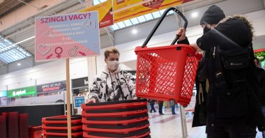 Two young men pick up their "single" shopping baskets at a French Auchan supermarket in Csomor town, Hungary, on Feb. 12, 202 (AFP Photo)