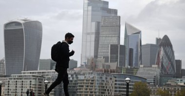 A man walks along the southern bank of the River Thames with the office towers of the City of London in the background, in London, Nov. 1, 2020. (AFP Photo)