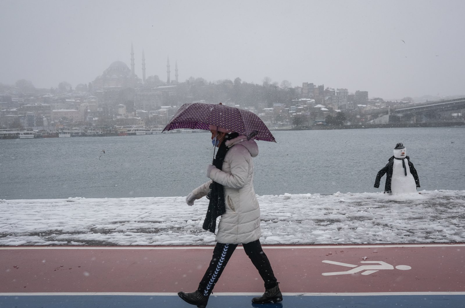 A woman passes by a snowman with Süleymaniye Mosque in the background on a snowy day during the lockdown in Istanbul, Turkey, on Feb. 14, 2021. (EPA Photo)