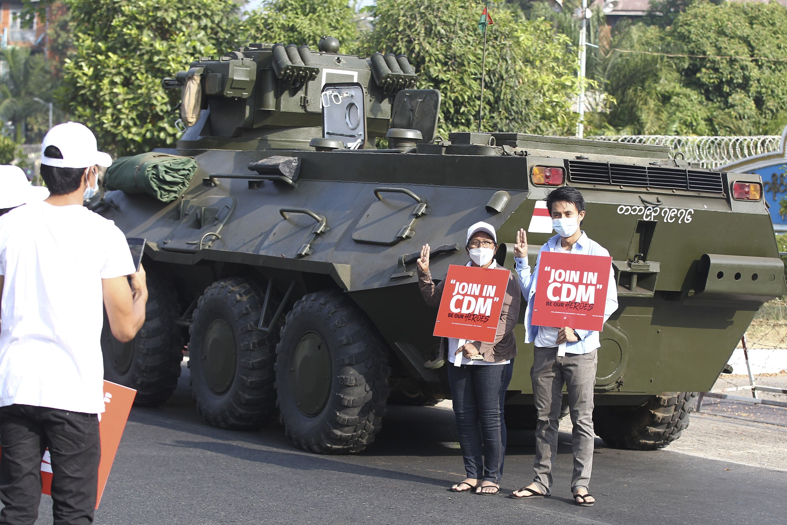 Anti-coup protesters flash the three-fingered salute and hold signs that read 'Join in CDM (Civil Disobedience Movement)' while they pose for a photo at the back of an armored personnel carrier deployed outside the Central Bank of Myanmar building in Yangon, Myanmar, Feb. 15, 2021. (AP Photo)