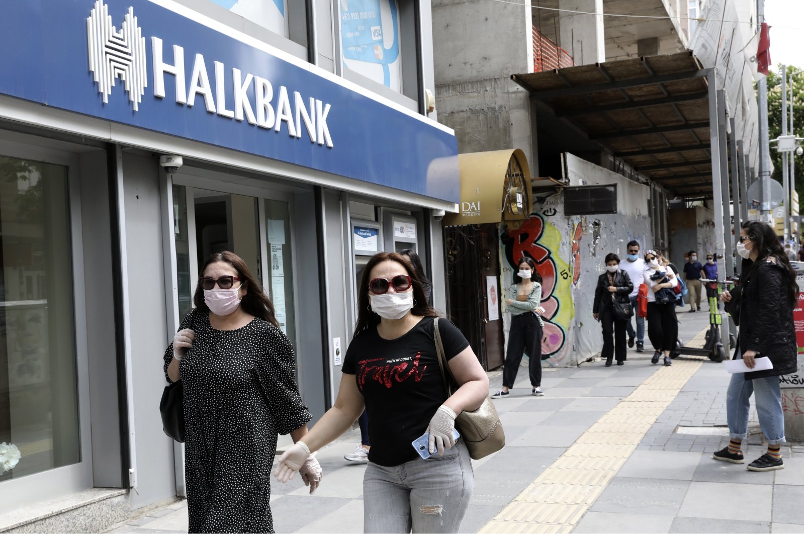 People wearing masks pass by the Halkbank branch in the capital Ankara, Turkey, May 11, 2020. (AP Photo)