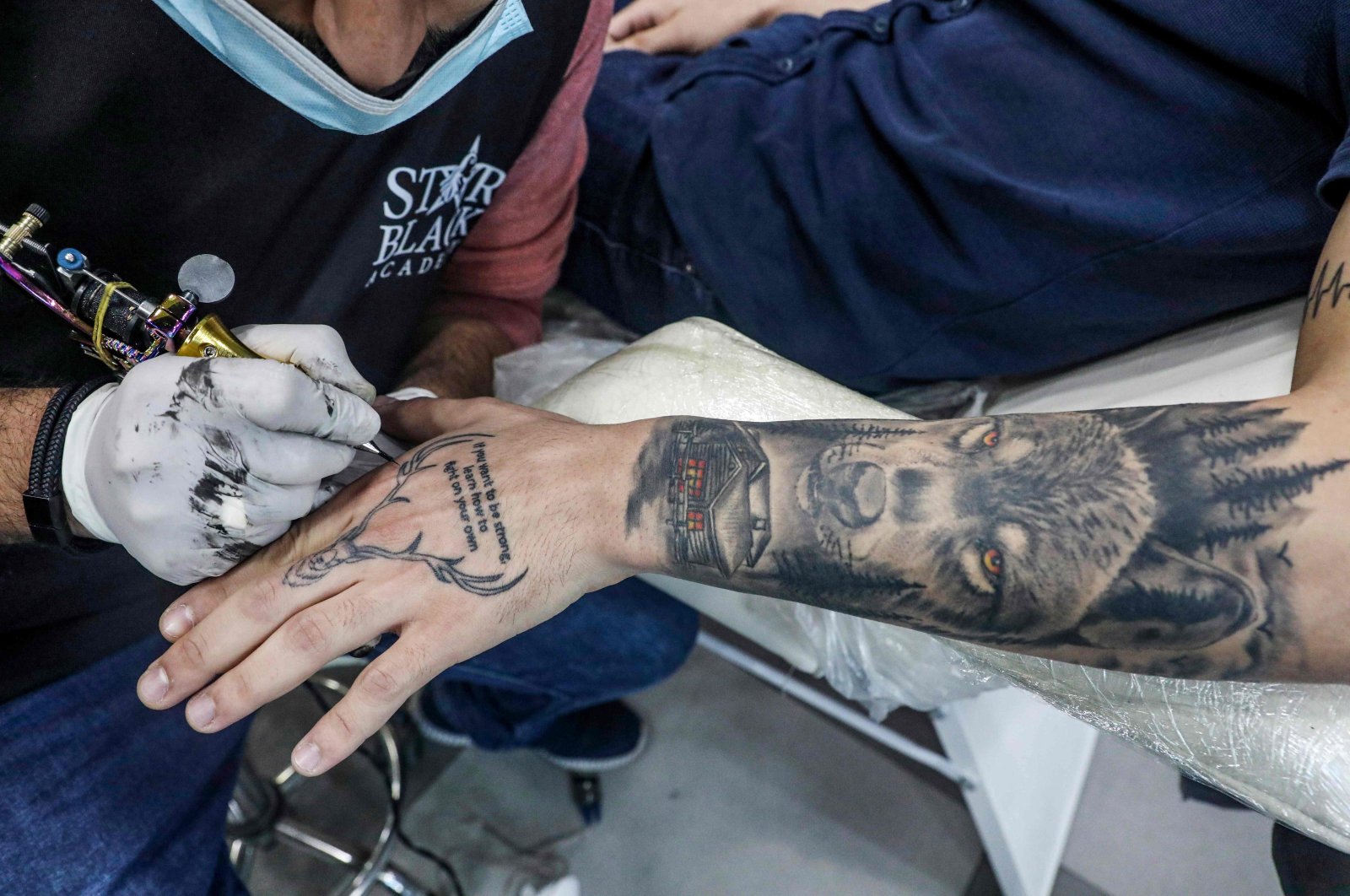 A tattoo artist applies a tattoo design of a stag's face with the English motto "if you want to be strong, learn to fight on your own" at his parlour in the city of Hebron in the occupied West Bank, on Jan 24, 2021. (AFP)