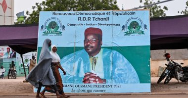 Women walk past a campaign poster of Niger's former president and presidential candidate, Mahamane Ousmane, ahead of Niger's presidential election runoff on Feb. 21, the capital Niamey, Feb. 18, 2021. (AFP Photo)