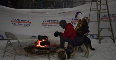 Zack Rosales, left, and his girlfriend Cynthia Thamez sit beside a backyard fire as their dog Alex sniffs at the snow beside them late in the evening in Abilene, Texas, Feb. 17, 2021. (AP Photo)