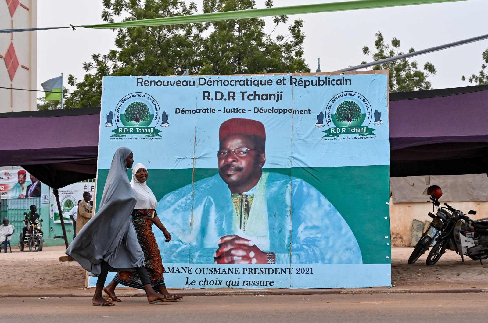 Women walk past a campaign poster of Niger's former president and presidential candidate, Mahamane Ousmane, ahead of Niger's presidential election runoff on Feb. 21, the capital Niamey, Feb. 18, 2021. (AFP Photo)