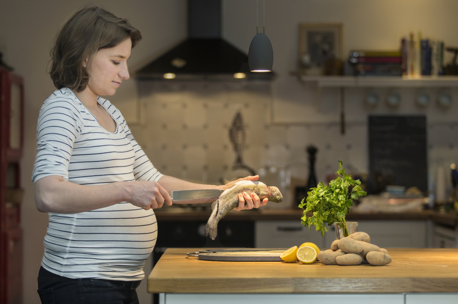 A 35-year-old pregnant woman cooks a fresh trout in the kitchen. (Getty Images)