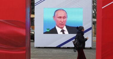 A woman walks past a screen showing Russian President Vladimir Putin during celebrations of the Defender of the Fatherland Day in Sevastopol, Crimea, Feb. 23, 2021. (REUTERS Photo)