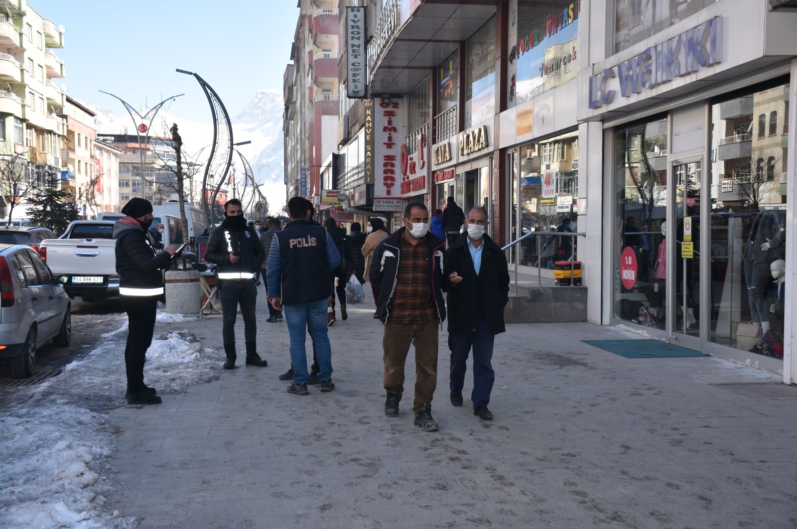 People wearing protective masks walk past police officers enforcing rules against the pandemic, in Hakkari, southeastern Turkey, Feb. 24, 2021. (AA Photo)