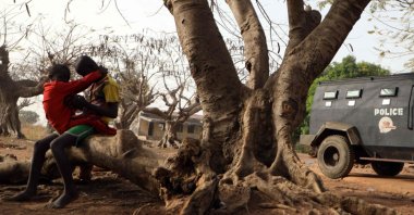 Children sit on a tree trunk next to an armoured personnel carrier stationed inside the Government Science College where gunmen kidnapped dozens of students and staffs, in Kagara, Rafi Local Government Niger State, Nigeria, Feb. 18, 2021 (Photo by Kola Sulaimon / AFP)