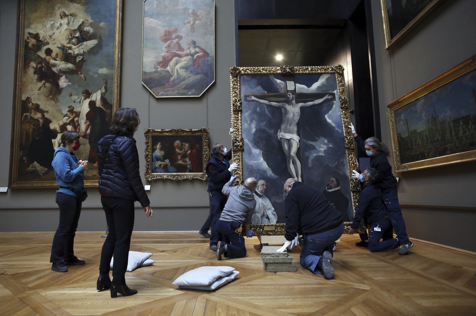 Workers handle a painting called 'Christ on the Cross Adored by Two Donors' by Spanish painter El Greco, as it returns from an exhibition at the Chicago Institute, in the Louvre museum, in Paris, Feb. 9, 2021. (AP Photo)