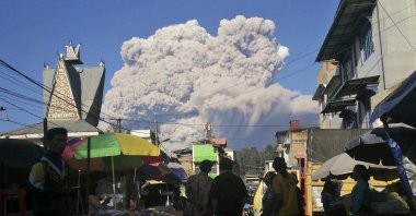 People watch as Mount Sinabung spews volcanic material during an eruption, at a market in Karo, North Sumatra, Indonesia, Tuesday, March 2, 2021. (AP Photo)