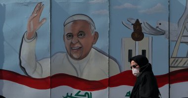A woman walks past a mural depicting Pope Francis on a concrete wall placed by Iraqi security forces to surround the Our Lady of Salvation Church during preparations for the Pope's visit in Baghdad, Iraq, Monday, March 1, 2021. (AP Photo)