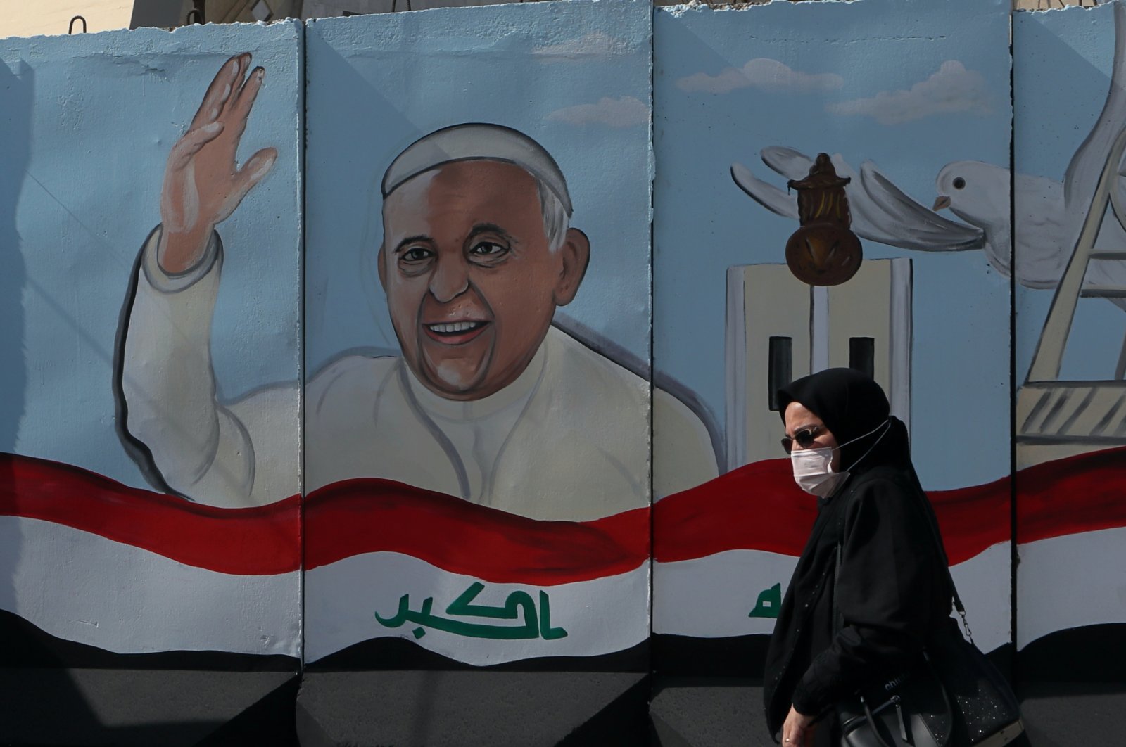 A woman walks past a mural depicting Pope Francis on a concrete wall placed by Iraqi security forces to surround the Our Lady of Salvation Church during preparations for the Pope's visit in Baghdad, Iraq, Monday, March 1, 2021. (AP Photo)
