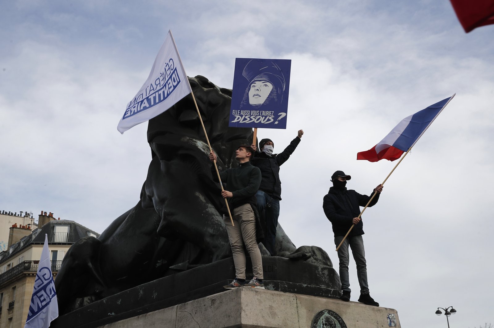 Supporters of the Generation Identity group wave flags while standing on a statue during a demonstration, Paris, France, Feb. 20, 2021. (AP Photo)