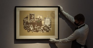 A staff member poses with "Morons (Sepia)" screenprint in colors, 2007, by Banksy during a press preview at Christie's in London, England, on Sept. 09, 2020. (Photo by WIktor Szymanowicz/NurPhoto via Getty Images)