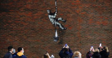 People take pictures of a mural by street artist Banksy on a wall at HM Reading Prison in Reading, Britain, March 1, 2021. (REUTERS)