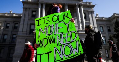 Monica Walsh holds a sign outside the Colorado State Capitol during a demonstration demanding answers about a lack of financial relief from the state in Denver, Colorado, Feb. 8, 2021. (AFP Photo)