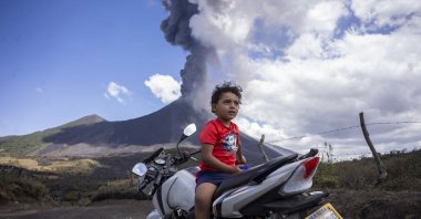A child sits on a motorcycle as the Pacaya volcano erupts in the background, viewed from San Vicente Pacaya, Guatemala, March 3, 2021. (AP Photo)