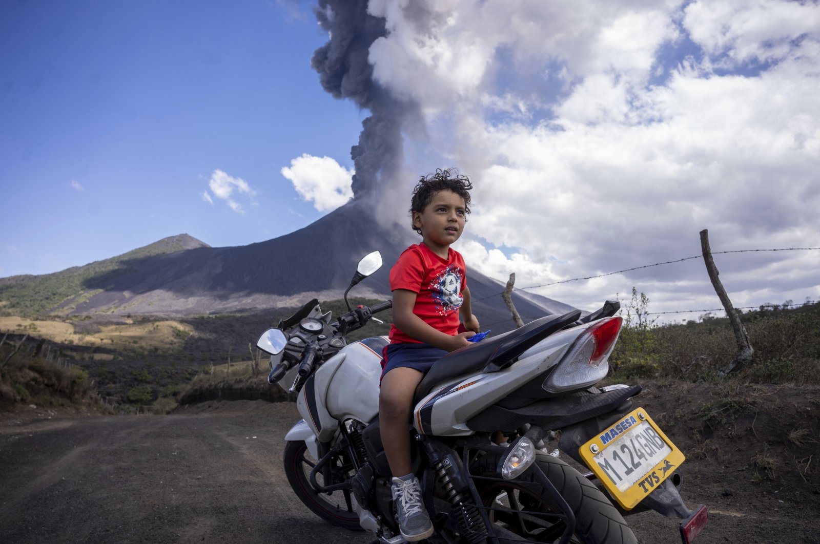 A child sits on a motorcycle as the Pacaya volcano erupts in the background, viewed from San Vicente Pacaya, Guatemala, March 3, 2021. (AP Photo)