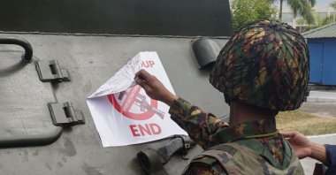 A soldier removes a protest sign denouncing the military coup stuck to an armoured vehicle outside the Central Bank of Myanmar in Yangon on Feb. 15, 2021. (AFP Photo)