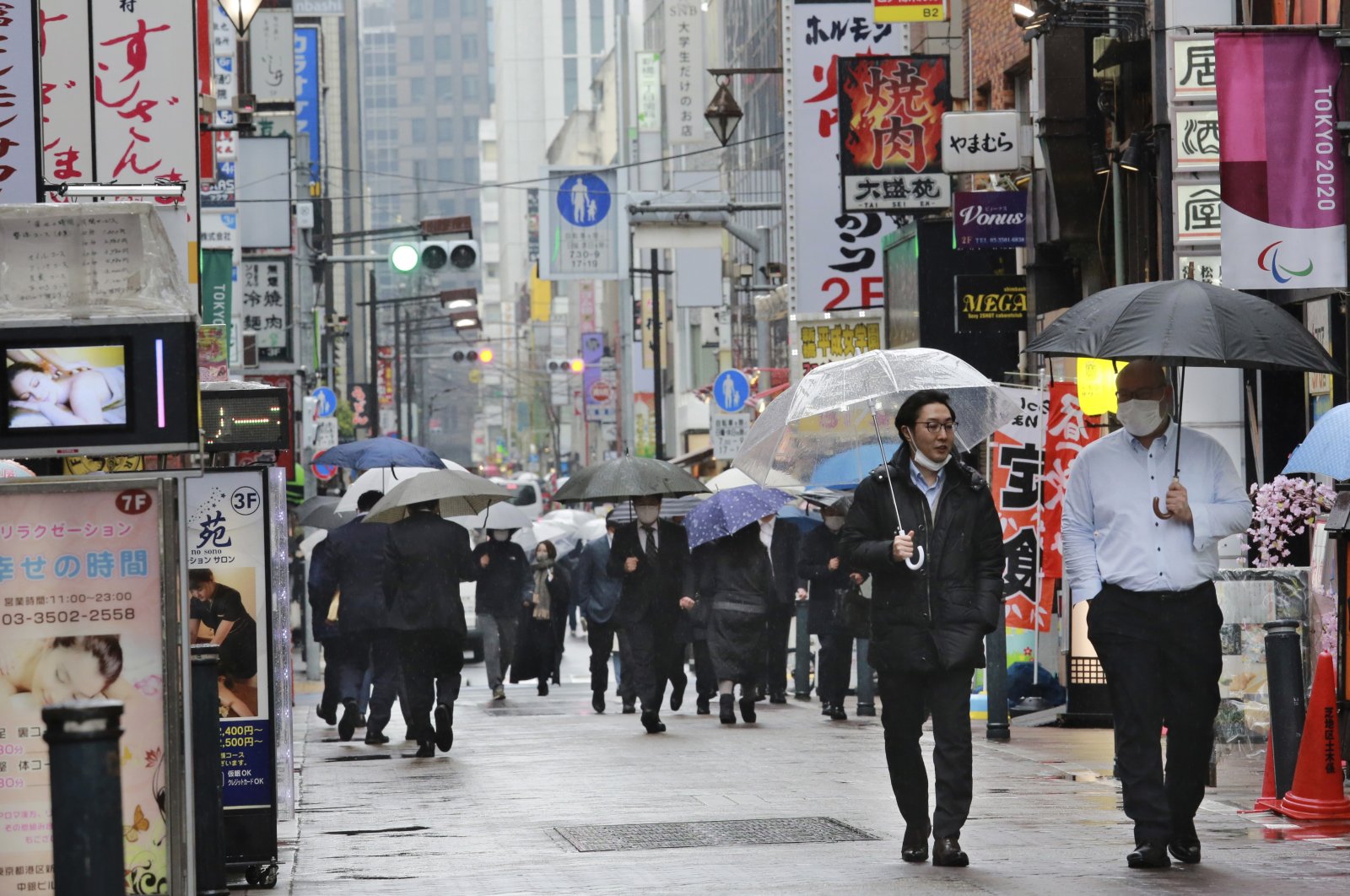 People wearing face masks to protect against the spread of the coronavirus walk on a street lined with bars and restaurants in Tokyo, March 8, 2021. (AP)