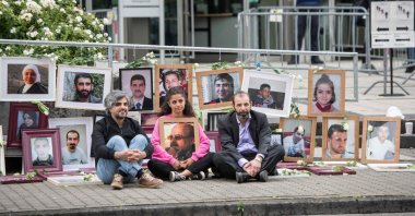 Syrian campaigner Wafa Mustafa (C) holding a picture of her father as she sits beside co-plaintiff, Syrian Oscar-nominated filmmaker Feras Fayyad (L), and Syrian human rights lawyer Anwar al-Bunni (R), in front of pictures of victims of the Syrian regime, during a protest outside the trial, in Koblenz, western Germany, June 4, 2020. (AFP)