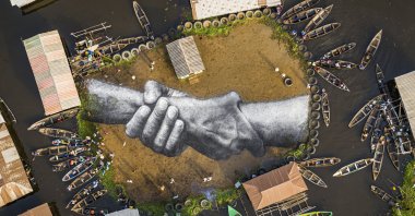 An aerial view shows a giant land art fresco by French-Swiss artist Saype, painted for the 10th step of his worldwide 'Beyond Walls' project in Ganvie, village on stilts, Benin, Wednesday, March 3, 2021. (Valentin Flauraud for Saype via AP)