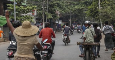 A woman on a motorbike flashes a three-fingered salute as a group of people flee after seeing the arrival of a convoy of soldiers and police officers to remove makeshift barricades made by anti-coup protesters in Mandalay, Myanmar, March 11, 2021. (AP Photo)