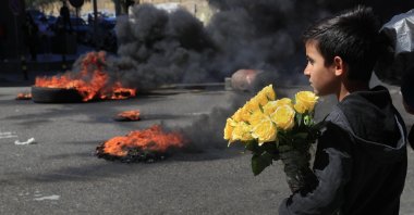 A Syrian boy who sells flowers on the street watches protesters burn tires to block a main road during a protest against the crash of the local currency, in Beirut, Lebanon, March 16, 2021. (AP Photo)