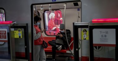 Commuters wearing face masks to help curb the spread of the coronavirus browse their smartphones inside a subway train in Beijing, China, Feb. 10, 2021. (AP Photo)